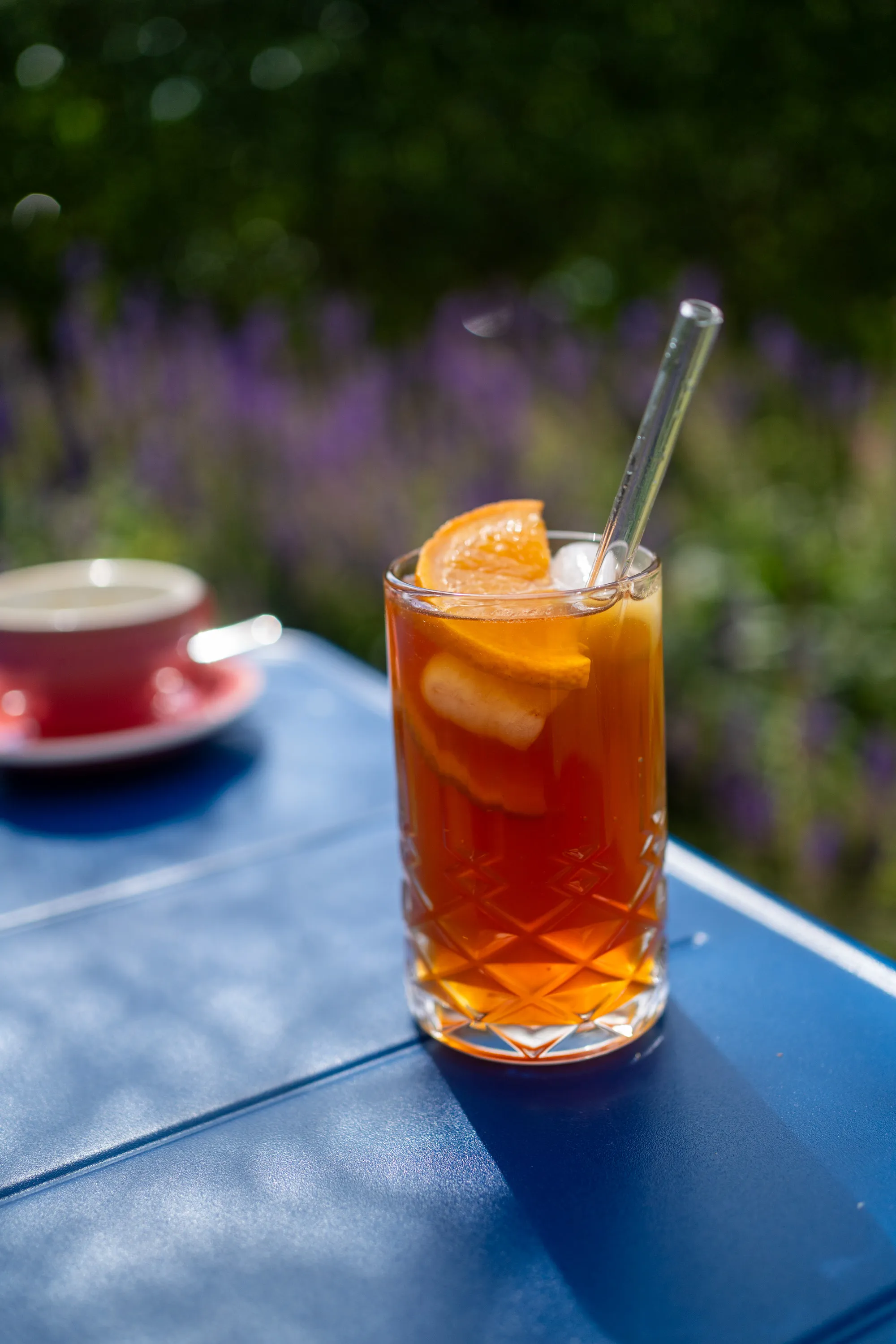 Hausgemachter Eistee mit Orangenscheibe und Glasstrohhalm auf einem blauen Tisch im Außenbereich